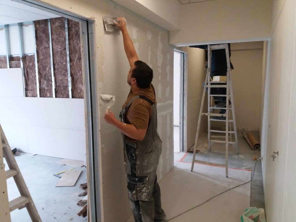 Stagiaire de l’asbl Boulot qui applique un enduit sur une cloison en plaques de plâtre dans le cadre d’une formation en techniques de rénovation à Bruxelles.